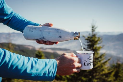 A selective focus shot of hands pouring tea into the cup in the mountains