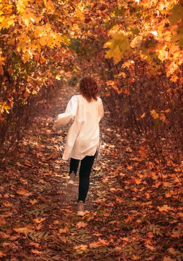 A rear view of a fashionable woman walking on an autumnal walkway