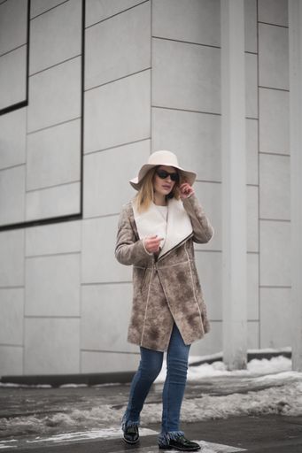 A vertical shot of an attractive blonde female wearing a warm leather coat, sunglasses, and a hat