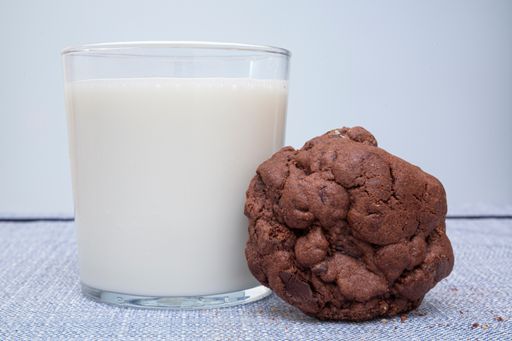 A selective focus shot of a tasty cookie and a glass of milk on a wooden table