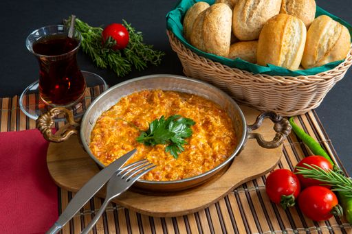 A top view shot of a Traditional Turkish dish menemen, made with eggs, tea, tomatoes, and bread