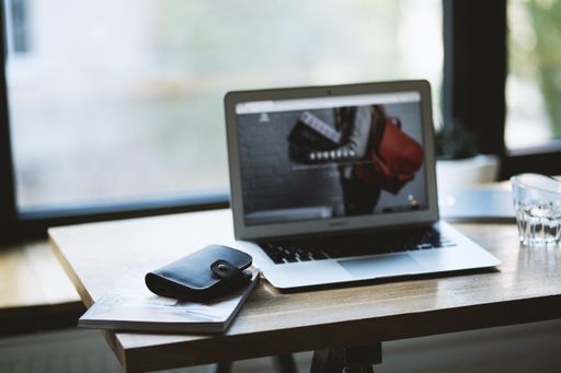 A selective closeup shot of a black wallet on a magazine near a gray laptop on a table