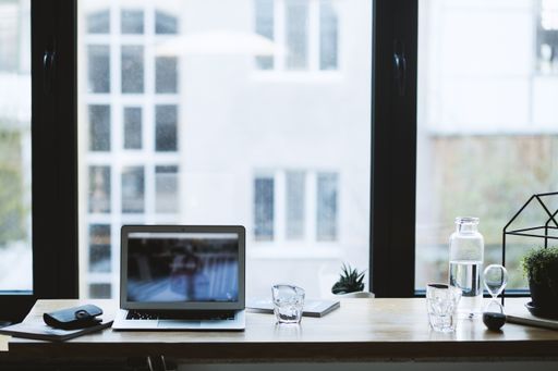 A selective closeup shot of a black wallet on a magazine near a gray laptop and glasses on a table
