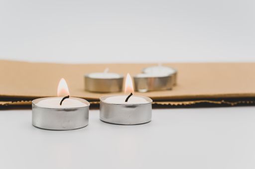 row of white scented wax tea lights on a white tabletop with copy space and folded paper bag