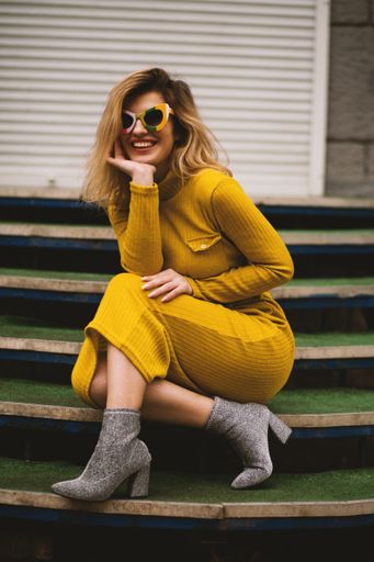 An attractive female model wearing a beautiful yellow dress and sunglasses posing near a staircase