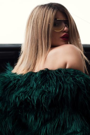 An attractive female model wearing a green fur dress and gold-framed sunglasses