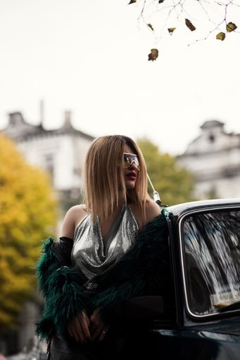A vertical selective shot of an attractive stylish and fashionable female model in a dress near a car