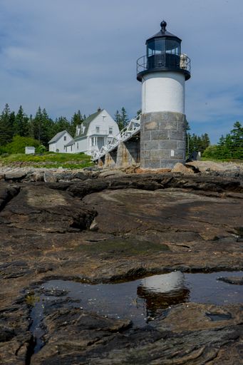 A vertical shot of a white house and Marshall Point Lighthouse with the background of pine trees, USA