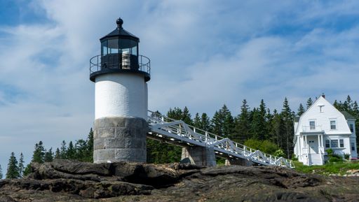 A beautiful white house and Marshall Point Lighthouse with the background of pine trees, Maine, USA