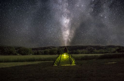 A green tent isolated in the field under a starry sky with Milky way galaxy