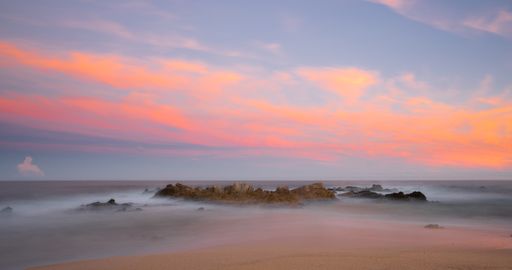 A beautiful soft pink sunset at the beach with the clouds hovering over the water
