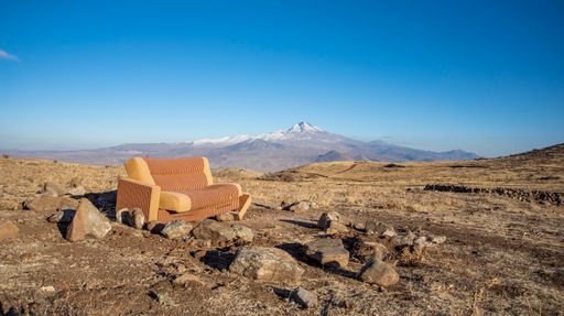 An old rusted couch in the middle of a big open field surrounded by mountains