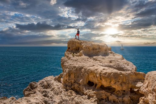 A man on the rocks at Praia do Carvoeiro horseshoe-shaped beach in Lagoa, Algarve, Portugal