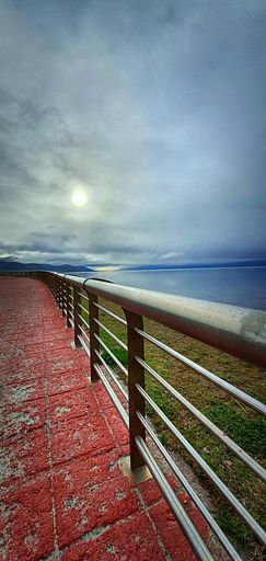 A vertical shot of metallic handrails on a ground painted red on a gloomy day with the background of the sea