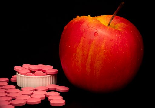 A healthy diet is the best preventive medicine. Pink pills next to a fresh red apple on black background. Healthy foods for vegetarians.