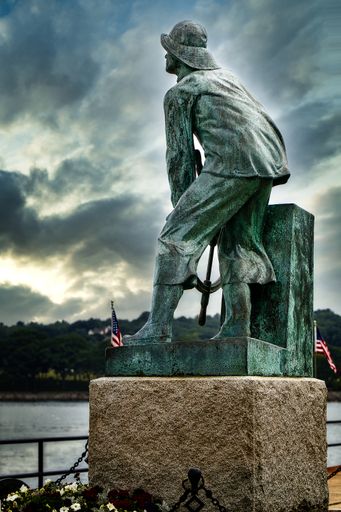 A vertical shot of a statue on a bridge under the cloudy skies