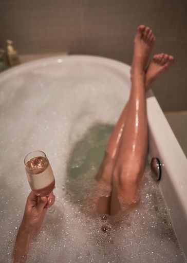 A vertical shot of a woman taking a bath while drinking a glass of champagne