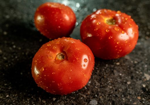 A closeup of fresh ripe tomatoes with water droplets on a black granite kitchen counter surface