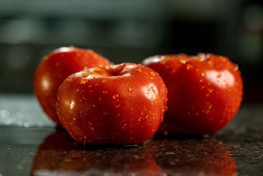A closeup of fresh ripe tomatoes with water droplets on a black granite kitchen counter surface