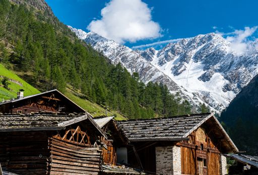 A closeup of wood cabins at the foot of an alpine mountain and a snowy mountain in the background, South Tyrol, Italy