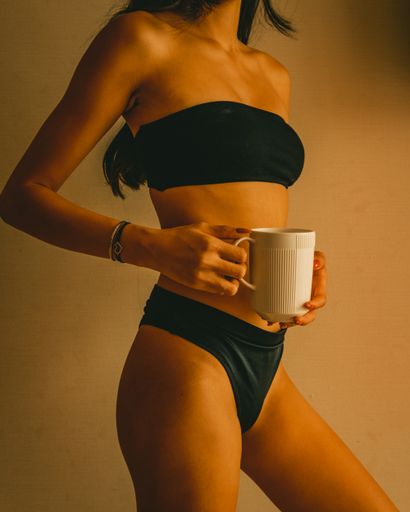 A vertical shot of a tan female in black lingerie holding a white mug