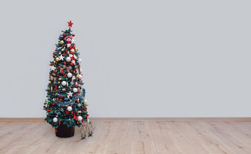 A decorated Christmas tree on a hardwood floor and a white wall background