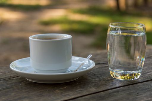A selective focus shot of white coffee mug and a glass of water on wooden table