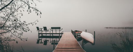 A breathtaking shot of a pier in a sea with a small boat near and some benches for seating