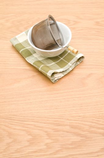 metal tea strainer with tea leaves in a ceramic bowl on a wooden background with text space