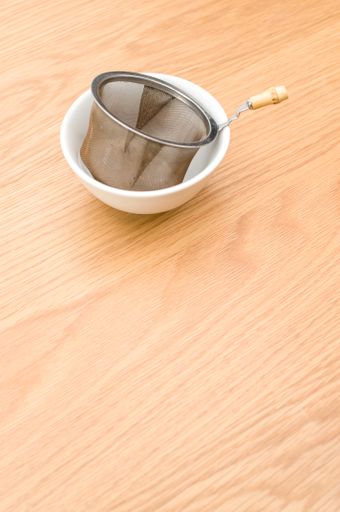 metal tea strainer with tea leaves in a ceramic bowl on a wooden background with text space
