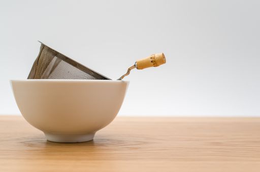 metal tea strainer with tea leaves in a ceramic bowl on a wooden background with text space