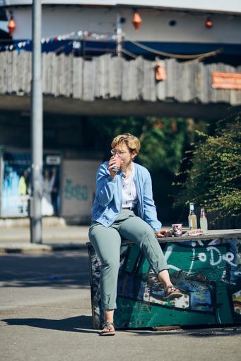 A vertical shot of a Caucasian woman drinking coffee and enjoying the sun on a street in Munich