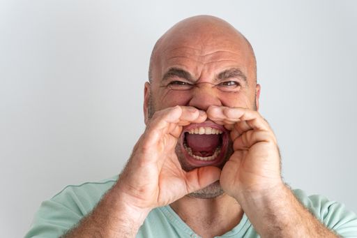 A close-up shot of a Caucasian man gesturing screaming with hands around open mouth