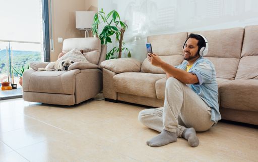 A horizontal shot of a male sitting on the floor, listening to music and smiling at the phone