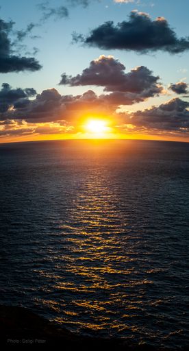 A vertical high angle shot of a seascape under the cloudy skies and the sunset