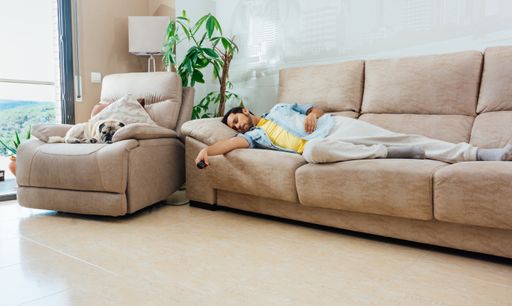 A young man in casual clothes sleeping on a sofa at home with a TV remote in hand