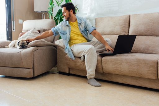 A young man in casual clothes petting his dog and using a laptop, working from home concept