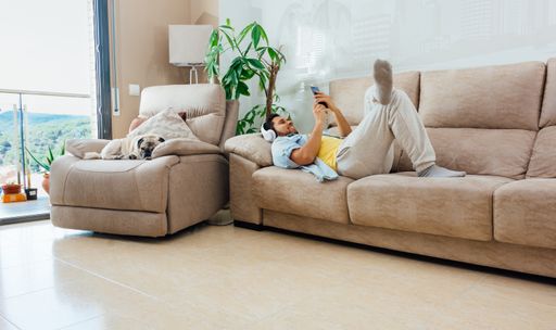 A young man listening to music with headphones while resting on the couch with his dog next to him