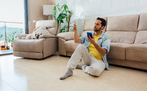 A male sitting on the floor of the living room with phone in one hand and a card in the other