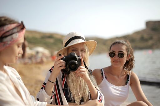 A selective focus shot of three female best friends, one taking a photo of the other at the beach