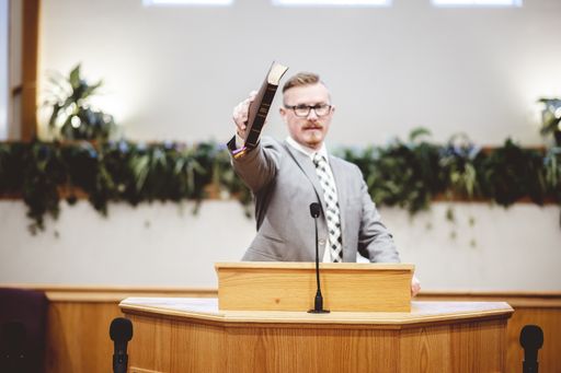 A male speaking near a wooden speech stand and holding a book in his hands- perfect for oratory, speech, lecturing concepts