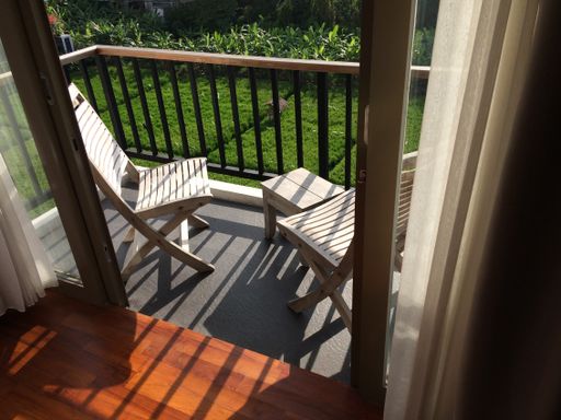 A beautiful shot of door to a balcony with wooden chairs near the metal fence over the grassy field