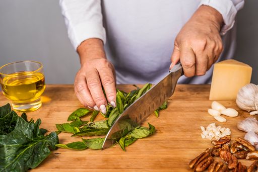 A close-up shot of an unrecognizable adult woman chopping basil with a kitchen knife