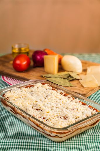 A vertical shot of homemade lasagna in a glass tray ready to cook with raw ingredients behind