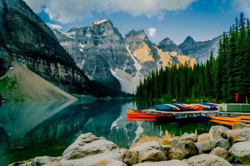 A calm lake with a pier and colorful boats surrounded by mountains and trees in Banff National Park, Alberta, Canada