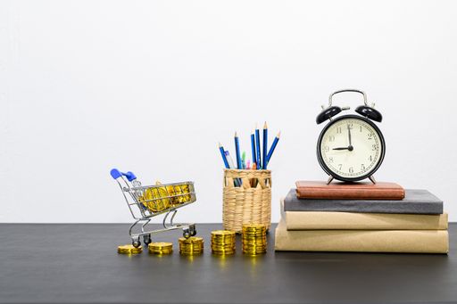 A stack of gold coins with miniature shopping cart and office supplies on a desk