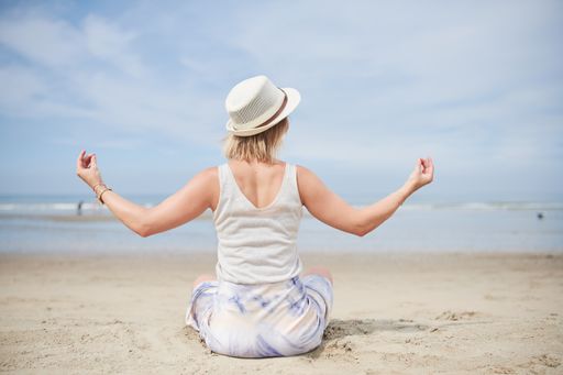 A back view of an unrecognizable woman meditating at a beach in summer