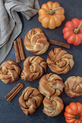 A vertical shot of freshly baked homemade pumpkin spice cinnamon rolls on a marble surface.