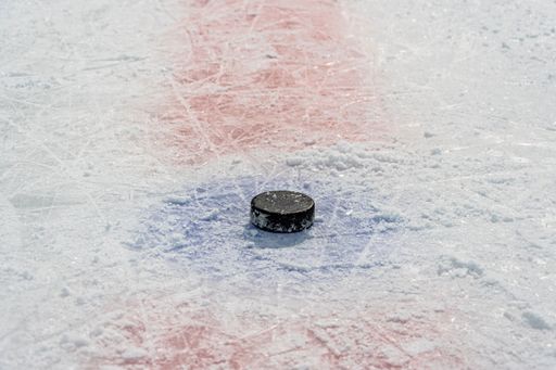 Clean empty ice hockey rink. Skate blade marks and snow crumbs. On surface of ice in center of throw-in circle is old game puck.