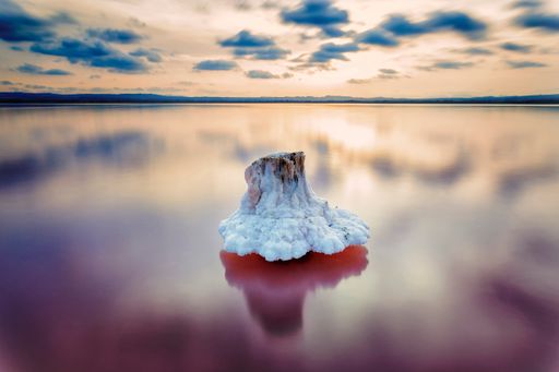 A scenic view of a sunset reflection in the water with a frosty stone under a cloudy winter sky in a long exposure - wallpaper